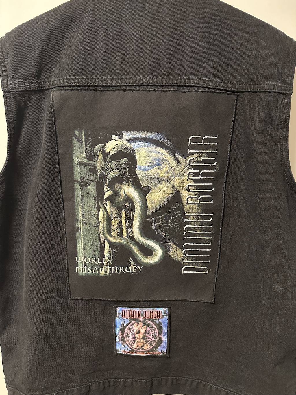 Foto der Kutte, sie hängt auf einem Kleiderbügel. Zu sehen der Rücken
          der Kutte, der bis auf einen dunklen, großen Backpatch und einen 
          kleinen, farbigen Patch mittig darunter noch leer ist. Der Backpatch
          zeigt einen Schädel aus dem Tentakel kommen, im Hintergrund ist ein
          Pentagramm angerissen. Entlang der rechten Seite steht, um 90º gegen
          den Uhrzeigersinn gedreht, "DIMMU BORGIR". Unter dem Schädel steht
          "WORLD MISANTHROPY".